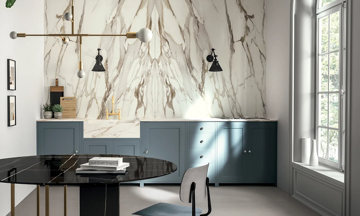 A modern kitchen featuring a stunning Calacatta Gold porcelain slab backsplash that extends from the countertop to the ceiling. The marble-look surface showcases elegant gold and gray veining, adding a luxurious touch to the space. The kitchen is well-lit, with sleek cabinetry and high-end appliances complementing the sophisticated design.