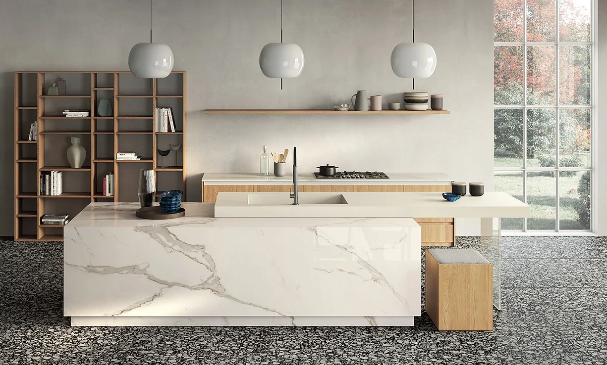 A stylish kitchen island featuring a Calacatta White porcelain slab with a striking waterfall edge. The surface showcases soft gray veining on a crisp white background, adding elegance and sophistication. The island serves as a focal point in the modern kitchen, complementing the surrounding sleek cabinetry and contemporary design elements.