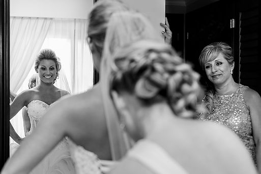 16-Black and white photo of smiling bride in mirror getting ready, with woman assisting.jp