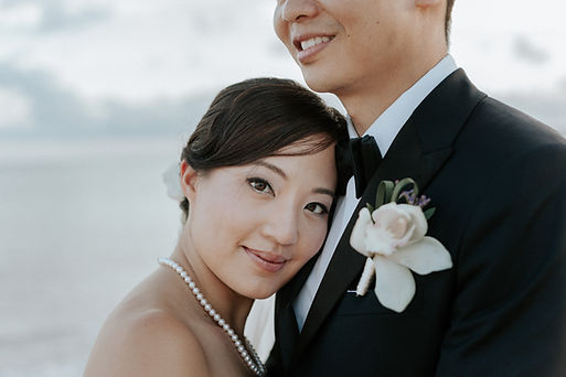 Close-up of a smiling Asian bride resting head on groom's shoulder