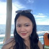 A young woman with long, dark hair smiles softly at the camera while on a boat.