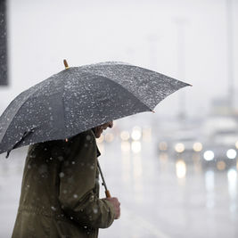 Person walking in heavy rain under umbrella during Canada weather alert 2026