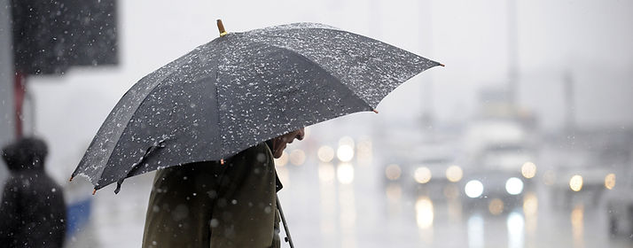 Ein Mann bei Regen mit Regenschirm der über eine Straße geht