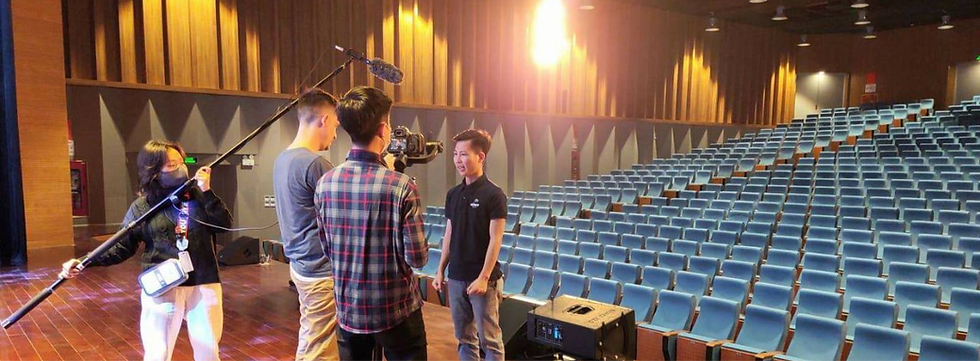 A video production team filming someone speaking on a stage in a large auditorium