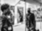 A man and a woman wearing masks in front of photographs hung outside