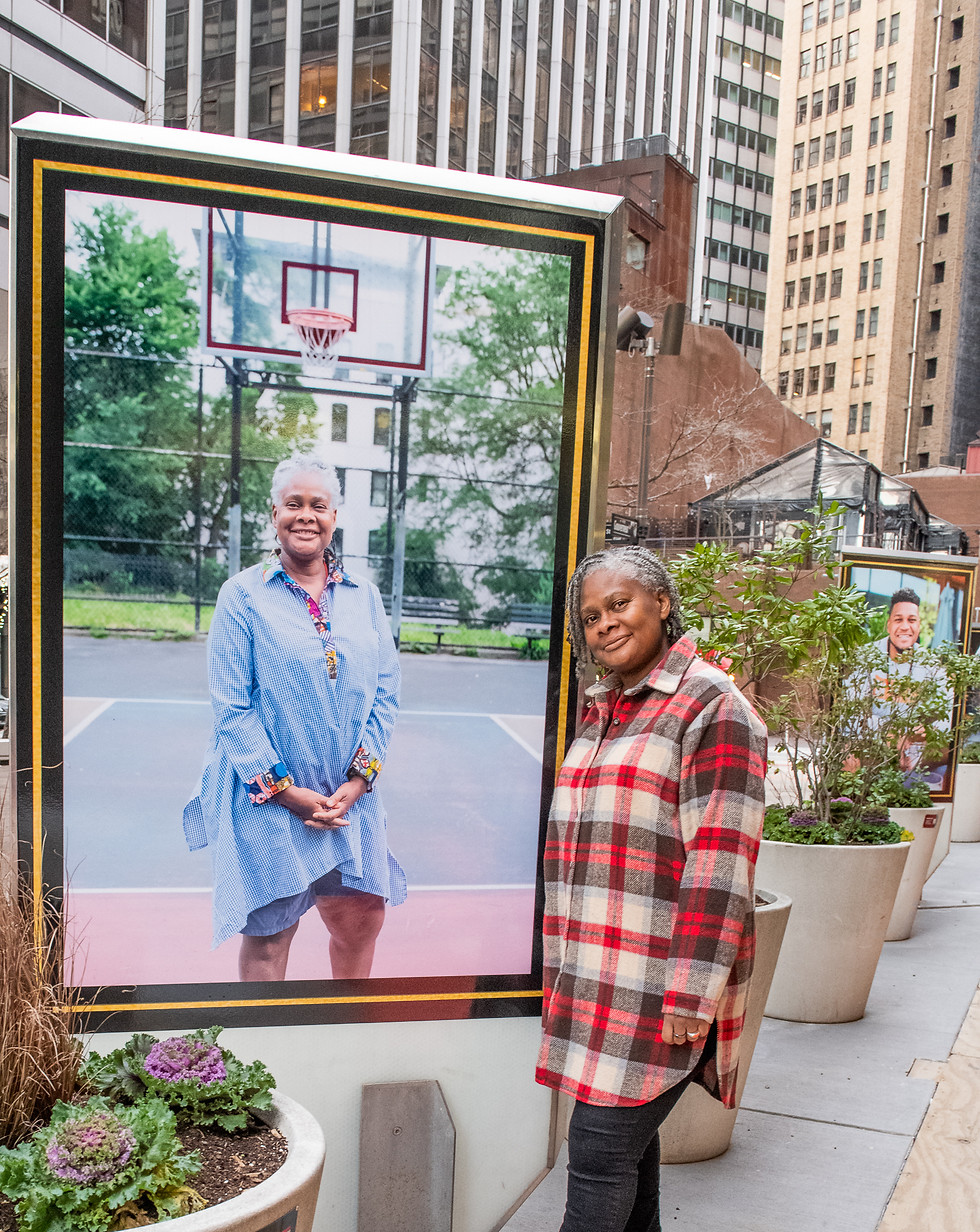 Shawn Batey portrait framed and displayed outside in city settings. Shawn stands next to her portrait