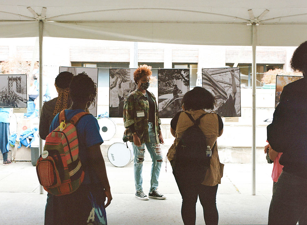 Woman stands in front of outdoor photo exhibition, audience looks on