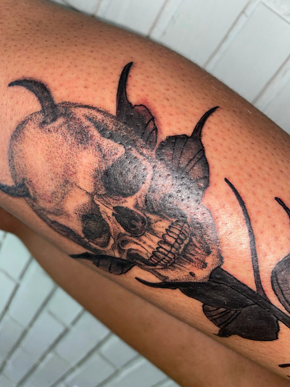 Tatuagem de caveira realista sombria com folhagens escuras na perna.