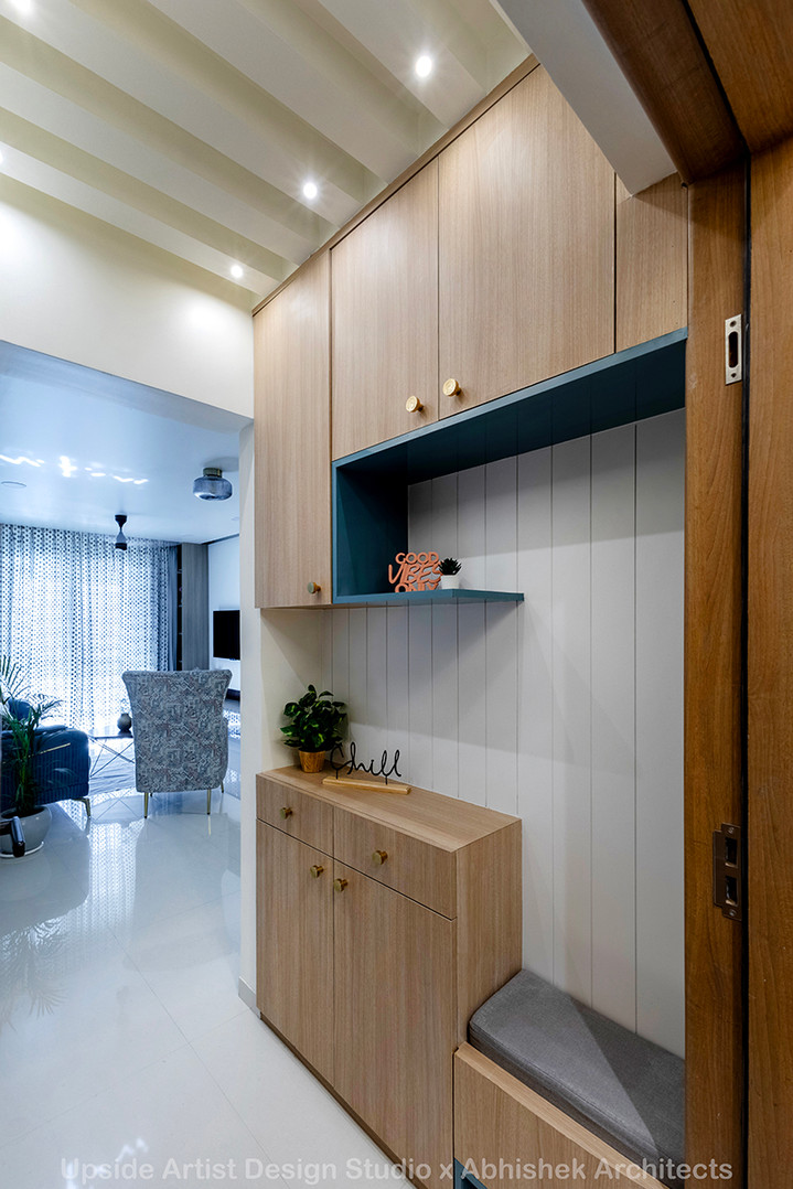 Minimalist wooden foyer storage unit with overhead cabinets, a teal open shelf displaying decor, a 'Chill' sign on a lower cabinet, and a grey cushioned bench.