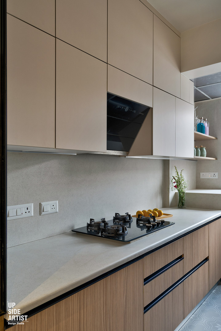 Straight-on view of a kitchen counter showcasing a black glass built-in gas stove hob on a grey stone countertop, beige upper cabinets, and fluted style wooden lower drawers.