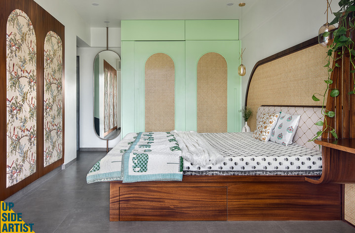 Complete view of a modern bohemian bedroom showcasing a low wooden bed, a large oval rattan wall accent, mint green wardrobes, and sliding wooden doors with a bird and flower print pattern.