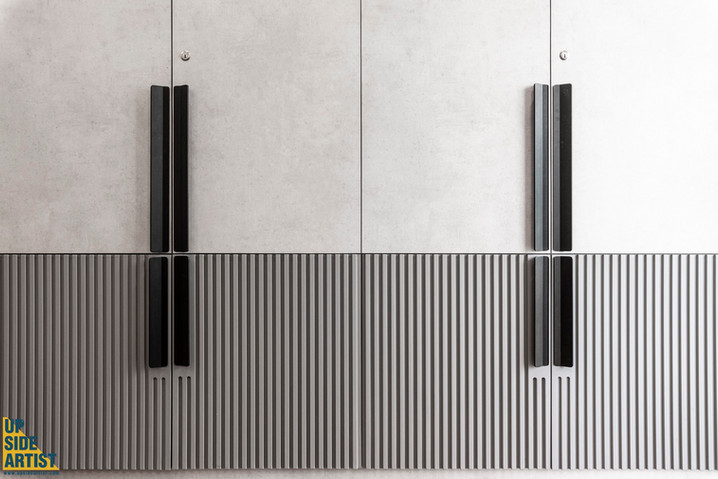 Close-up of wardrobe cabinet doors detailing the contrast between a smooth concrete texture and a gray ribbed fluted panel, centered by vertical black handles.
