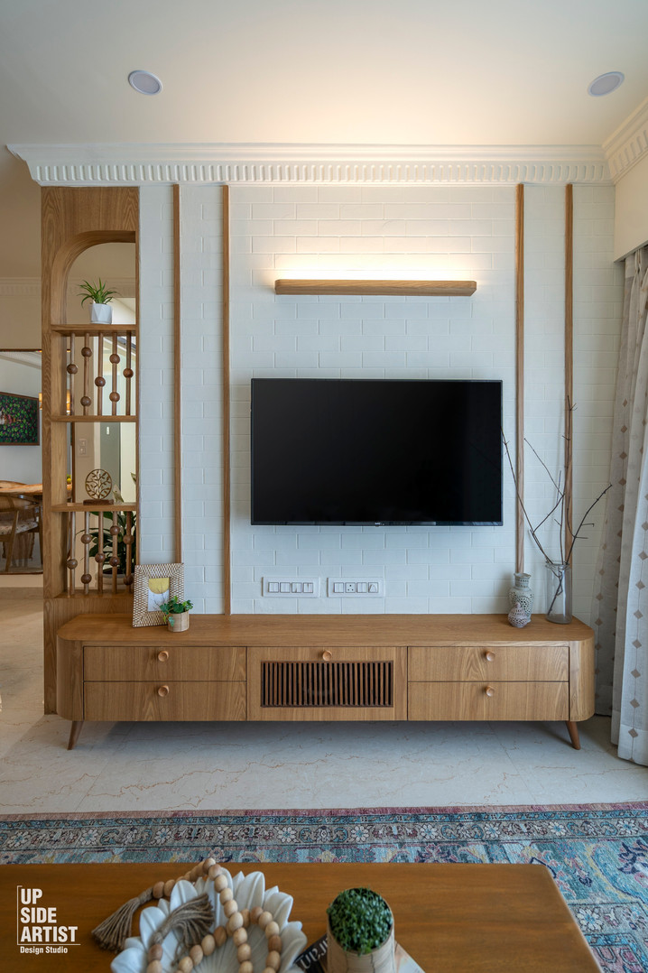 Living room media center featuring a wall-mounted TV over a long oak wood console table, a white brick backdrop with wood slats, and a built-in wooden display partition shelf.
