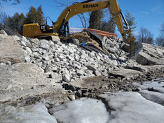 Excavator with Behan Construction logo working at shoreline rock site