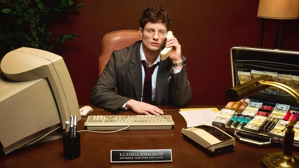 A person in a suit talks on a phone at a desk with a retro computer, makeup, and cash. Plaque reads "E.L.Fino & Schmarnes." Brown background.
