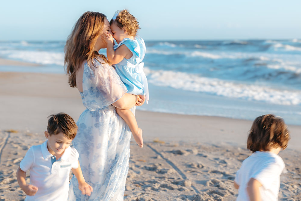 Mom holding toddler, two kids playing on a sunny beach