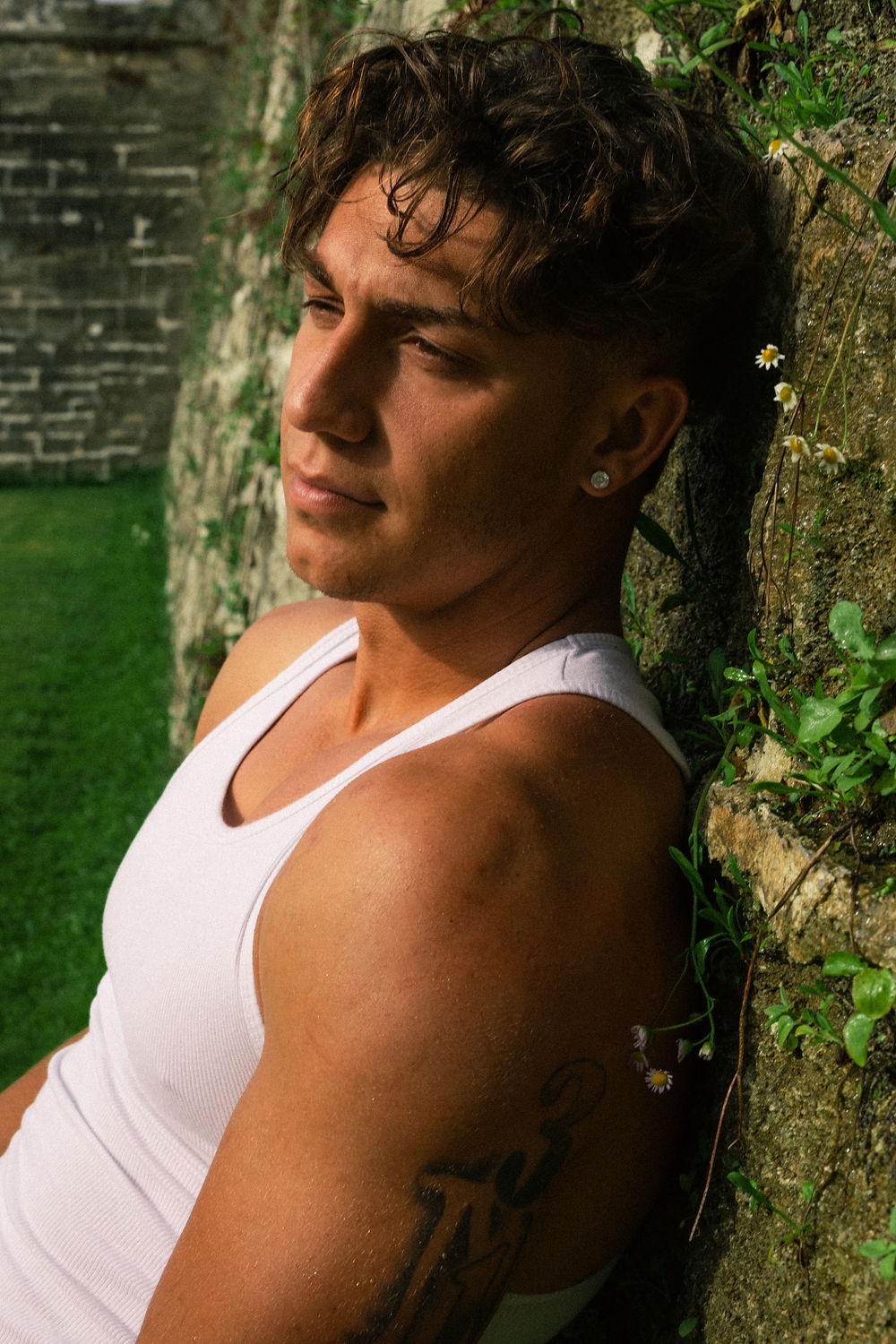 Young man in white tank top leaning on a stone wall