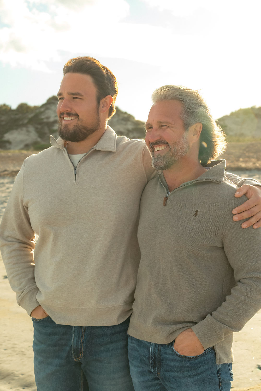 Two men smiling on a beach at sunset