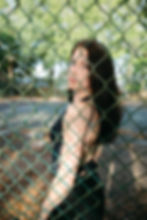 Young woman looking back through a chain-link fence.