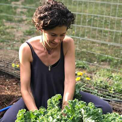 A photo of Tracy Gary seated in a sunny vegetable garden gazing down and a beautiful green kale plant
