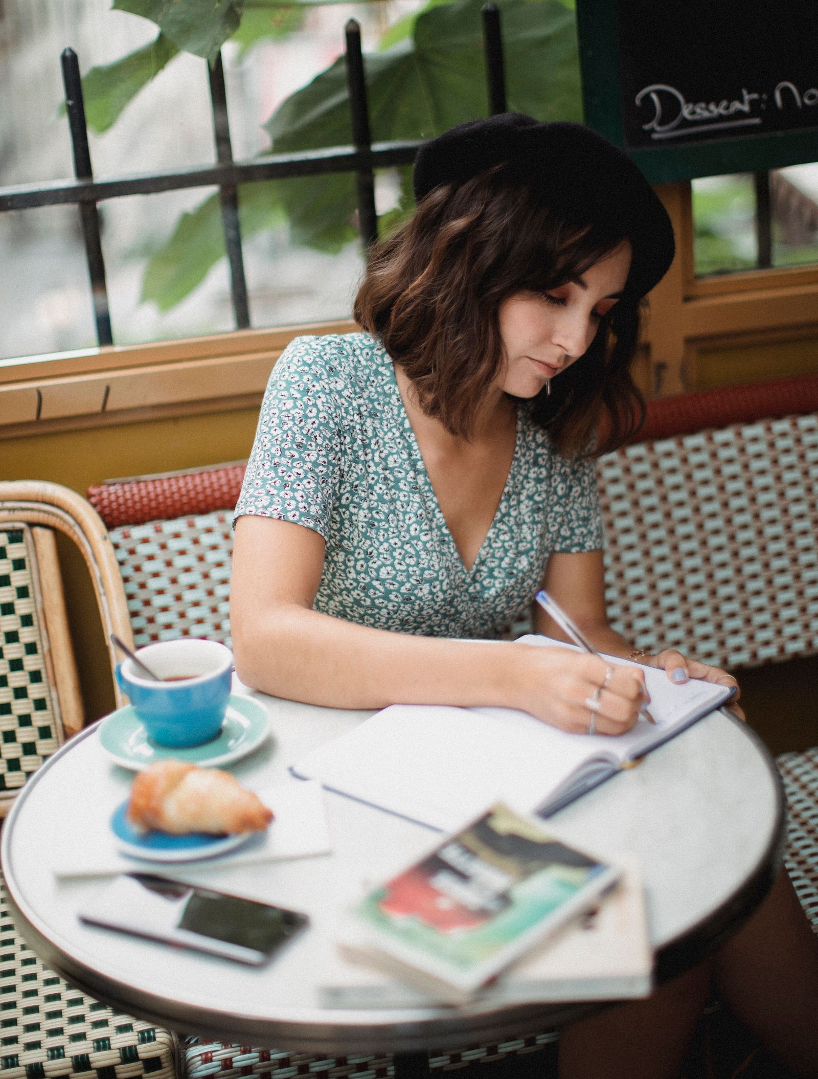 A woman writing in her journal at a café table with a cup of coffee