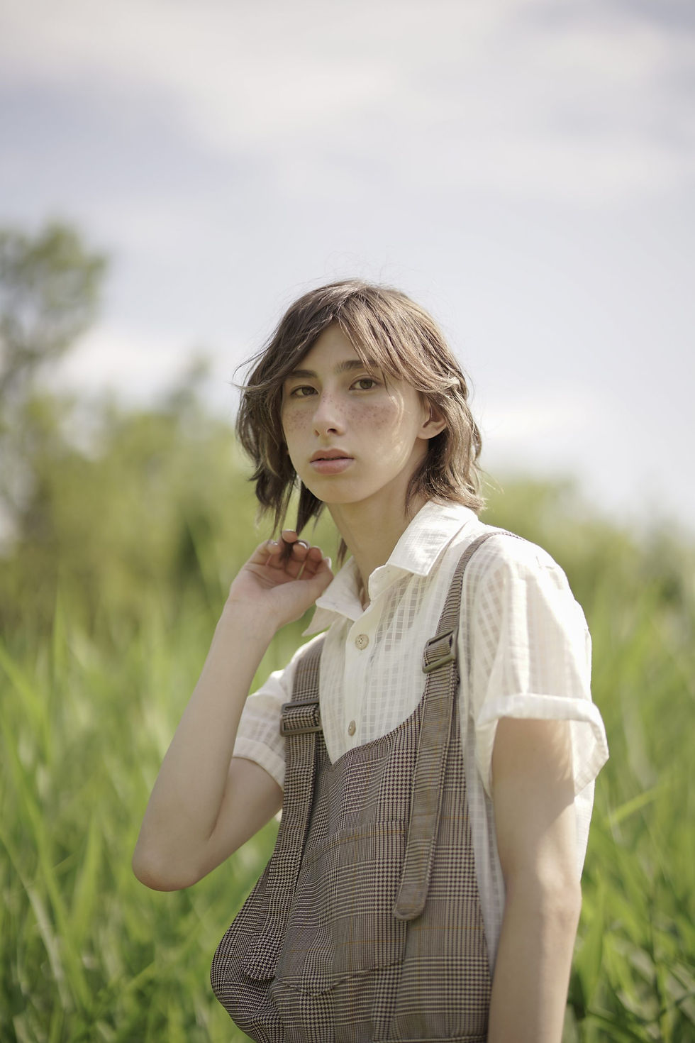 Thumbnail: Young person in overalls standing in a sunny grassy field.