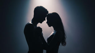 Silhouetted couple facing each other intimately under a spotlight, creating a romantic and moody atmosphere with a soft, dark gradient background.