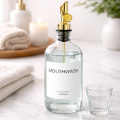 Minimalist glass mouthwash dispenser set with stainless steel pour spouts, shot glasses, waterproof labels, and funnel styled on a modern bathroom counter.