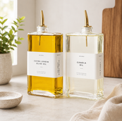 Minimalist glass oil and vinegar dispenser set with gold pour spouts, reusable labels, and a funnel, styled as a modern kitchen countertop essential.