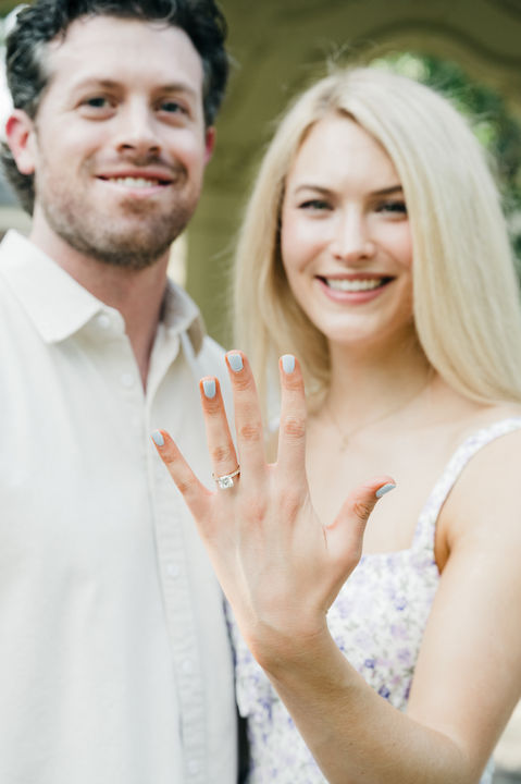 Smiling bride-to-be showing engagement ring in Dallas garden.