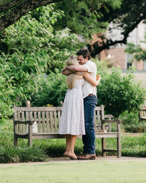 Engaged couple embracing and kissing in a lush Dallas park setting.
