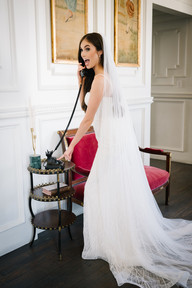 Bride in wedding dress standing beside chair in historic interior at The Mason Dallas during bridal portraits