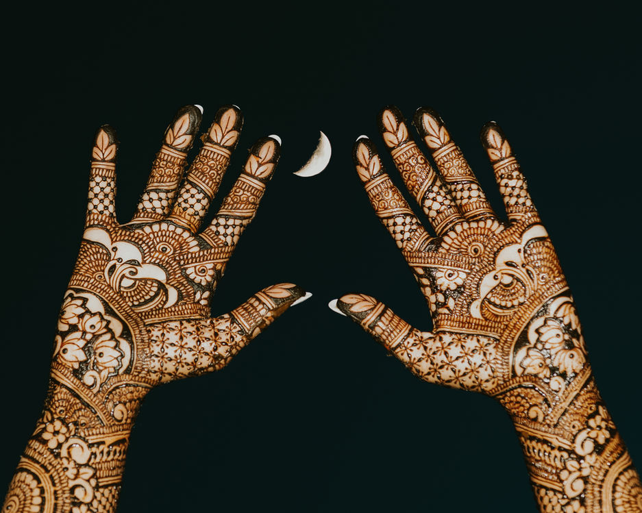 Bride’s hands with intricate henna designs raised beneath a crescent moon
