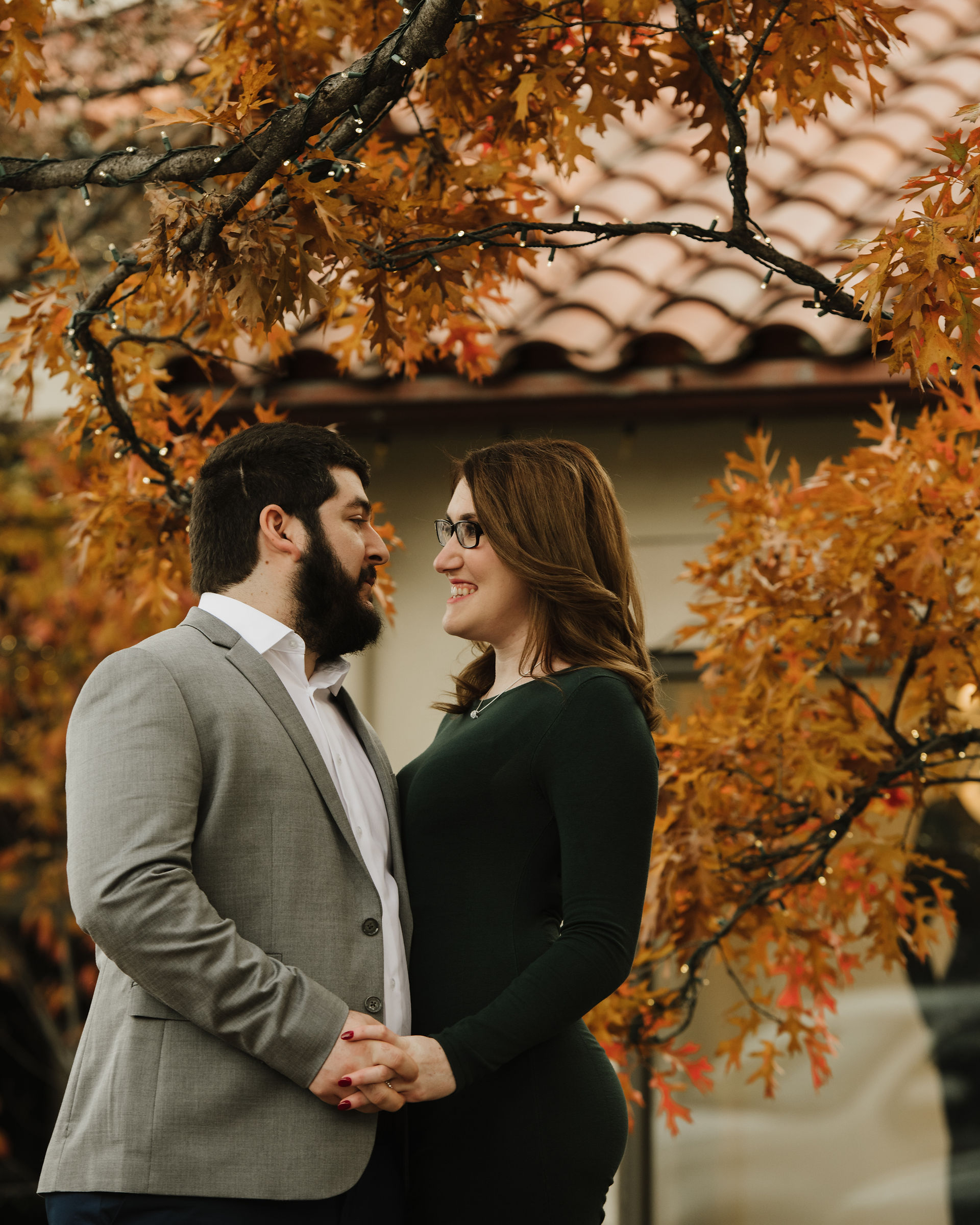 Couple holding hands beneath autumn tree at Highland Park Village Dallas.
