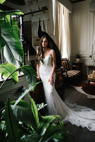 Bride in wedding dress standing by window with plants during bridal portraits at The Mason Dallas