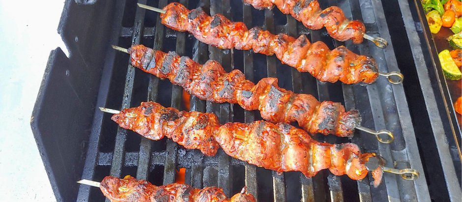 Grilled Boti Kebab skewers with browned meat on a BBQ grill. Vegetables visible on the side, creating a savory, outdoor cooking vibe.