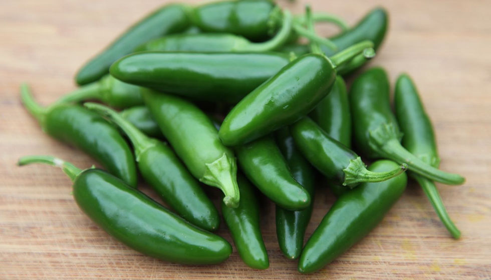 Pile of glossy green jalapeño peppers on a wooden cutting board, fresh and ready for cooking.