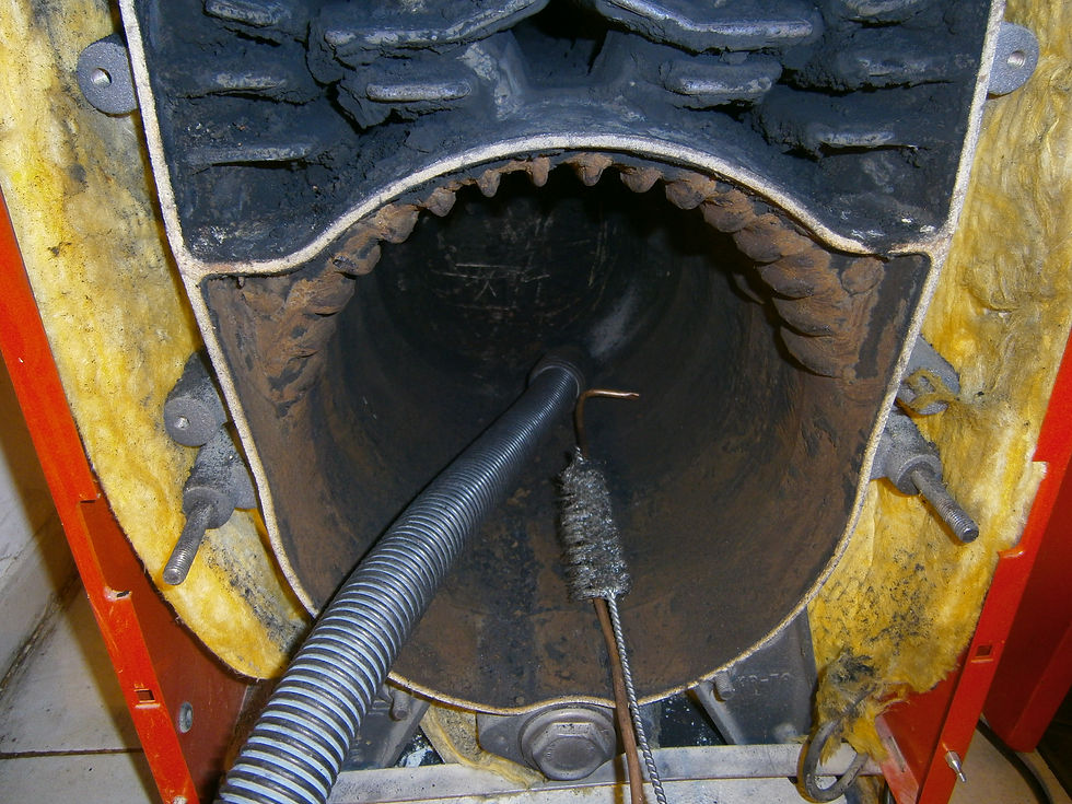 Close-up of a rusty boiler interior being cleaned with a brush and vacuum hose. Yellow insulation and red panels surround the opening.