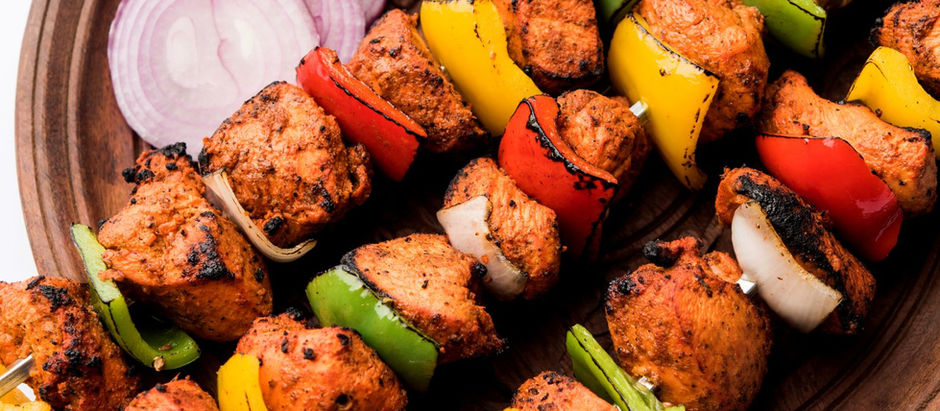 Grilled Shashlik skewers with colorful peppers and chicken on a wooden plate, served with sliced onions, lime, and a bowl of green dip.