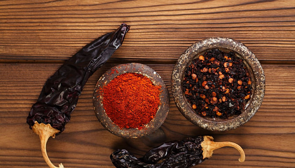 Dried chilies with red chili powder and pepper flakes in small bowls on a wooden table, warm rustic food prep scene