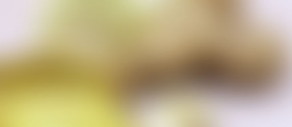 Sliced ginger, whole ginger root, garlic cloves, and a sliced onion on a light wooden surface. The scene conveys freshness.