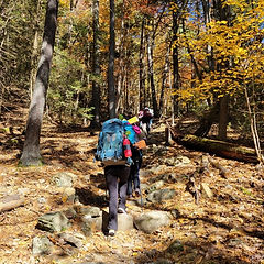 Backpacker carrying a full pack on leaf-covered trail—beginner-friendly wilderness hiking weekend