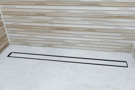 Matte black linear shower drain installed in a light gray stone tile floor in Vaughan.