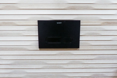 Matte black Duravit dual-flush plate installed on textured wood-look wall tiles in a Vaughan bathroom renovation.