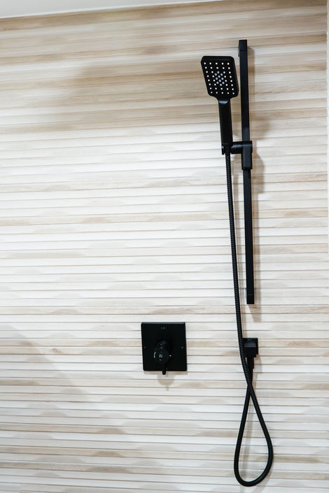 Matte black hand shower and pressure-balanced valve installed on wood-texture wall tile in Vaughan.