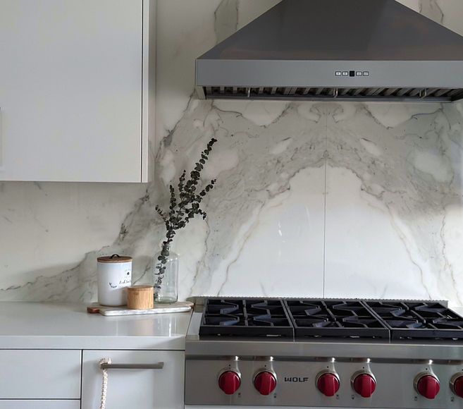 Modern white kitchen with high-end Wolf cooktop, red knobs, bookmatched backsplash, and sleek design.