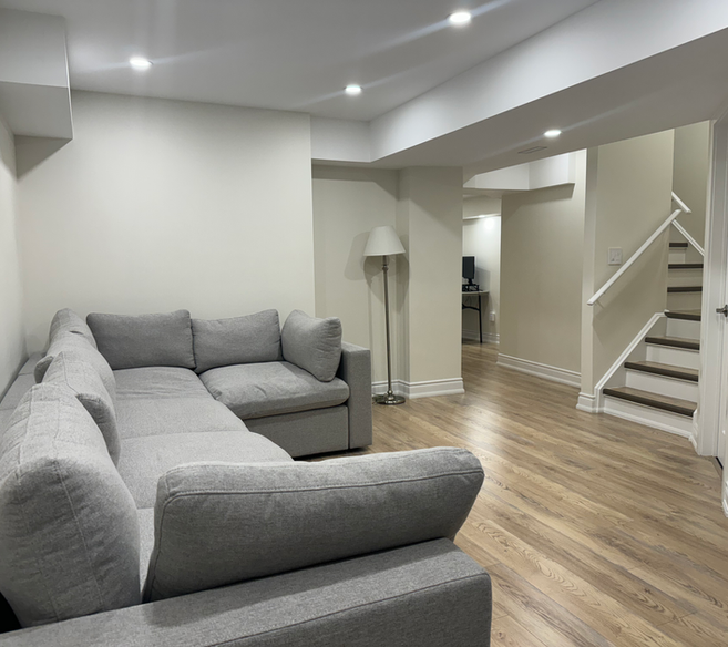 Modern basement with natural wood flooring, grey couch, brand new stairs, and complete renovation in York Region, including Thornhill and Vaughan.