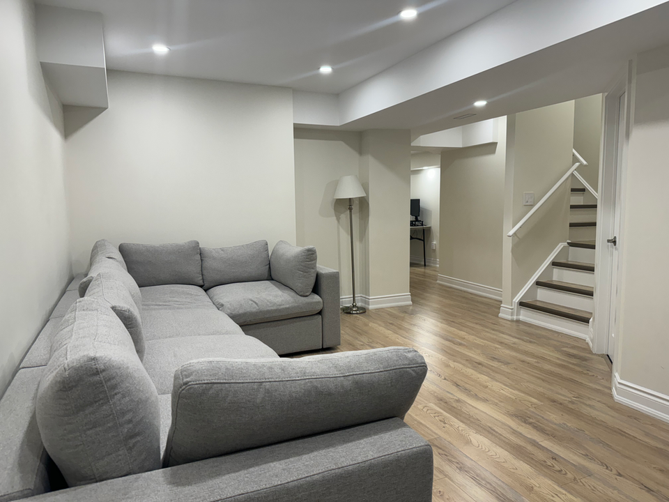 Modern basement with natural wood flooring, grey couch, brand new stairs, and complete renovation in York Region, including Thornhill and Vaughan.
