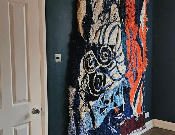 Tamessa Capall Mara Wall Hanging by Ryka Design shown hung on deep teal wall in hallway displaying large-scale figurative composition in navy, cream and burnt orange hand-tufted wool with organic fringing edges