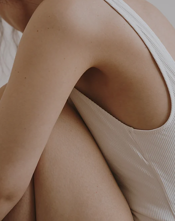 A woman is alone dressed in a singlet sitting down on the floor hugging herself. She looks to be contemplating something important.